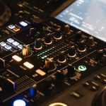 A detailed view of a DJ deck showcasing knobs, dials, and lighting effects in a nightclub setting.