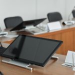 A modern conference room setup featuring digital monitors and microphones on a wooden table.