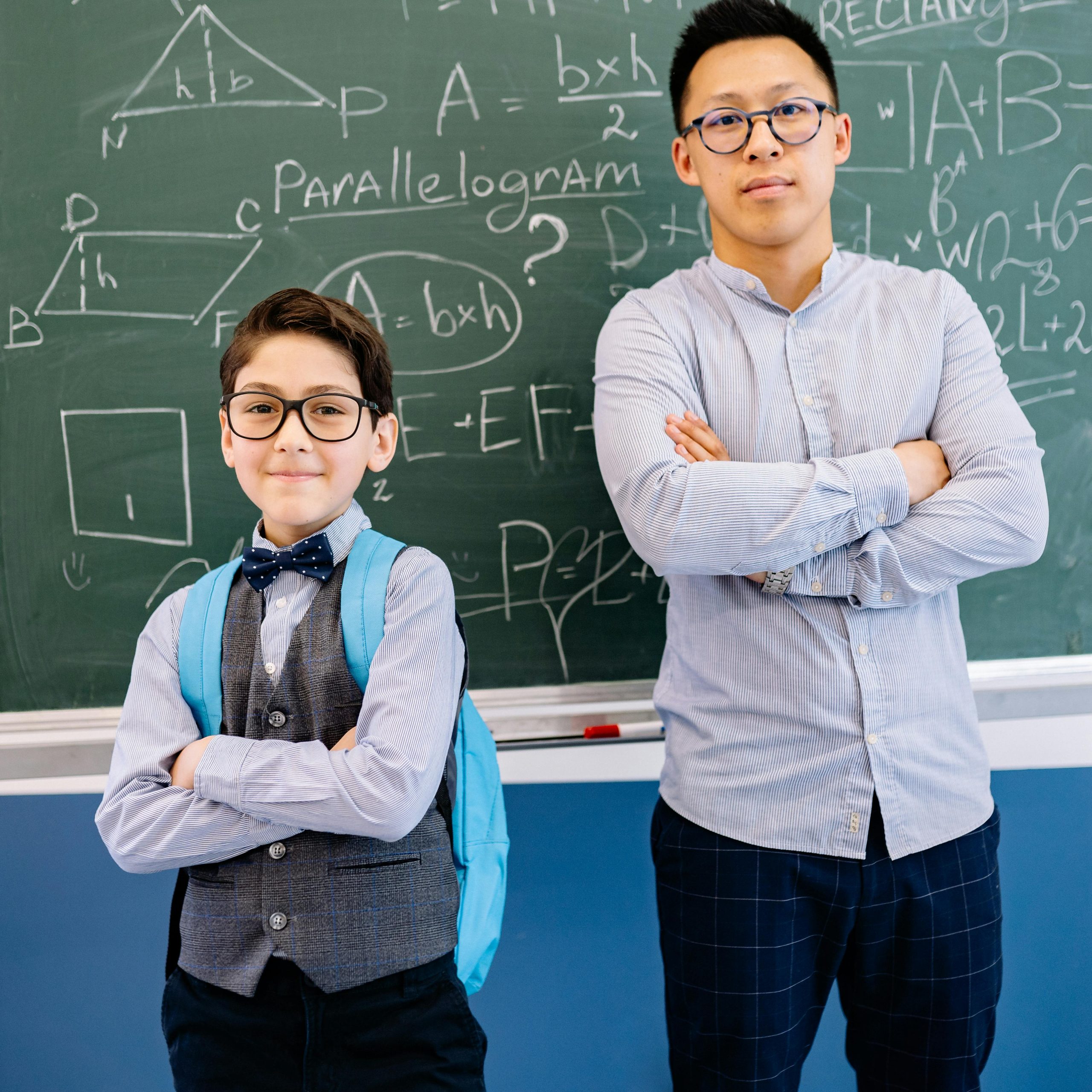 Teacher and student posing confidently in front of a blackboard with math equations.